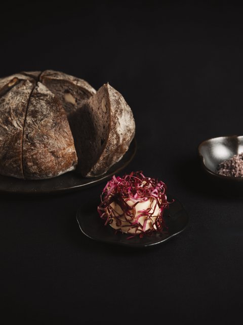 Bilder aus der Sportalm Rundes Brot auf Teller mit Butter und Salz vor dunklem Hintergrund