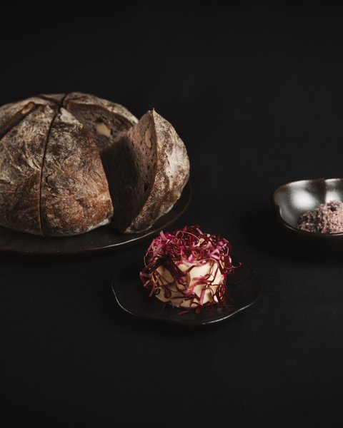 Bilder aus der Sportalm Rundes Brot auf Teller mit Butter und Salz vor dunklem Hintergrund