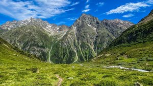 Hiking hotel in Pitztal: nature adventurers, ahoy! Green mountain trail under blue sky with snow-capped peaks