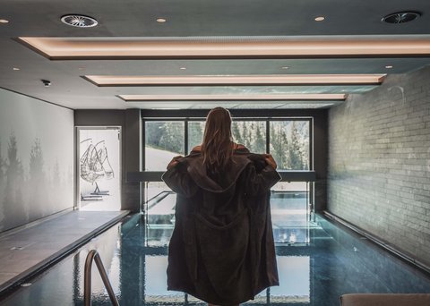 Pictures from Sportalm Woman in bathrobe by indoor pool with panoramic window and mountain view