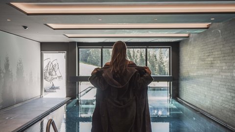 Bilder aus der Sportalm Frau in Bademantel vor Innenpool mit Panoramafenster und Bergblick