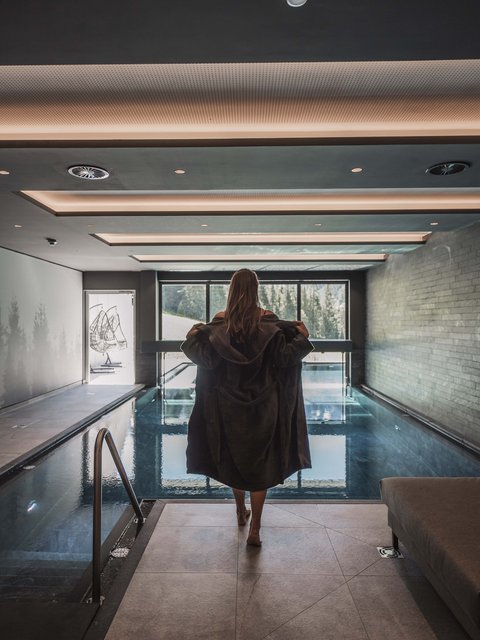 Bilder aus der Sportalm Frau in Bademantel vor Innenpool mit Panoramafenster und Bergblick