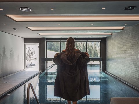 Bilder aus der Sportalm Frau in Bademantel vor Innenpool mit Panoramafenster und Bergblick
