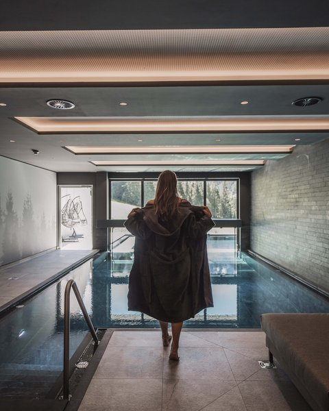 Bilder aus der Sportalm Frau in Bademantel vor Innenpool mit Panoramafenster und Bergblick