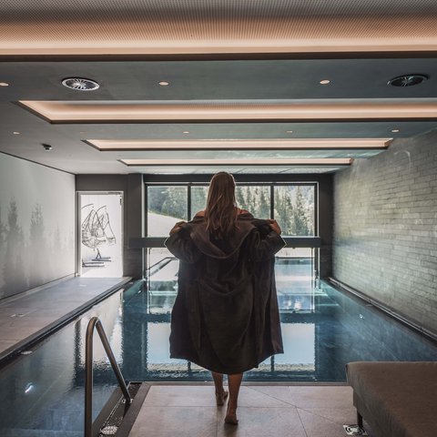 Bilder aus der Sportalm Frau in Bademantel vor Innenpool mit Panoramafenster und Bergblick