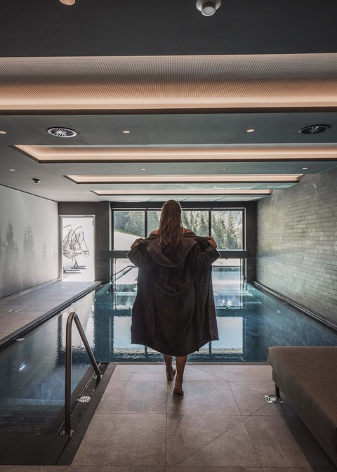 Pictures from Sportalm Woman in bathrobe by indoor pool with panoramic window and mountain view