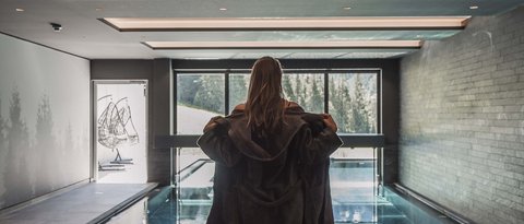Bilder aus der Sportalm Frau in Bademantel vor Innenpool mit Panoramafenster und Bergblick