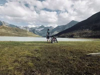 Radfahrer blickt auf Bergsee und Alpen unter bewölktem Himmel