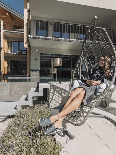 Bilder aus der Sportalm Frau entspannt in einem Hängesessel auf einer Terrasse mit moderner Architektur