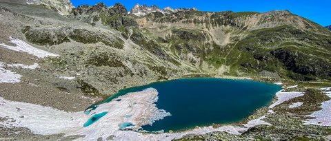 Bilder aus der Sportalm Bergsee mit schmelzendem Schnee und felsigem Gelände unter klarem blauem Himmel