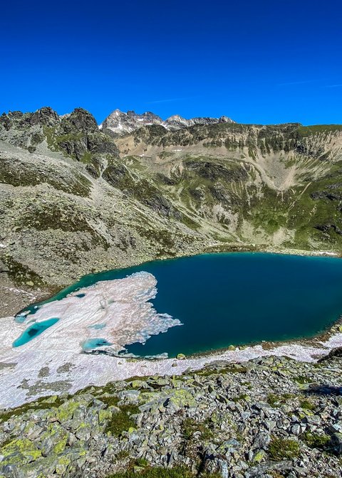 Pictures from Sportalm Mountain lake with melting snow and rocky terrain under clear blue sky