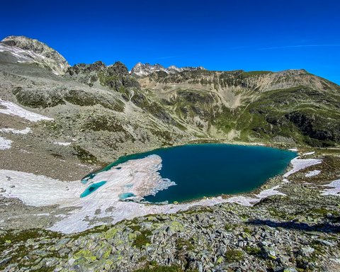 Bilder aus der Sportalm Bergsee mit schmelzendem Schnee und felsigem Gelände unter klarem blauem Himmel