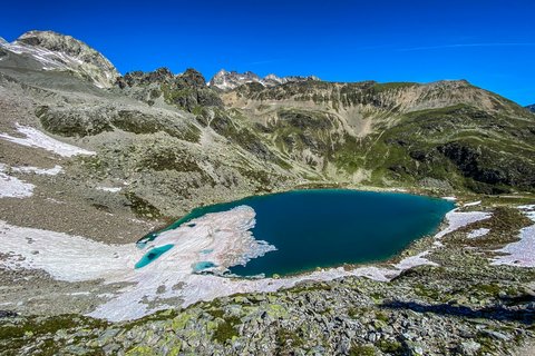 Bilder aus der Sportalm Bergsee mit schmelzendem Schnee und felsigem Gelände unter klarem blauem Himmel