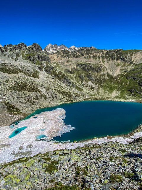 Pictures from Sportalm Mountain lake with melting snow and rocky terrain under clear blue sky