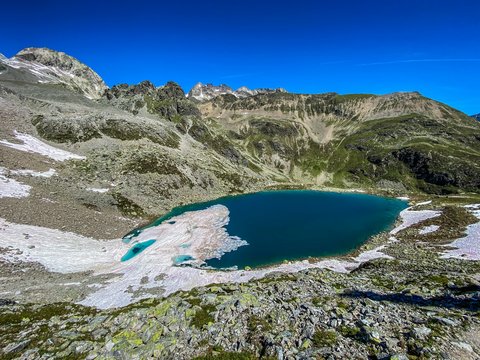 Bilder aus der Sportalm Bergsee mit schmelzendem Schnee und felsigem Gelände unter klarem blauem Himmel
