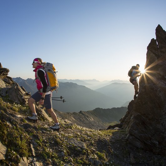 Hiking hotel in Pitztal: nature adventurers, ahoy! Two hikers climbing rocky mountain path at sunrise