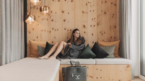 Bilder aus der Sportalm Frau entspannt auf Holzcouch mit Kissen und Wandlampen