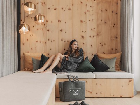 Bilder aus der Sportalm Frau entspannt auf Holzcouch mit Kissen und Wandlampen