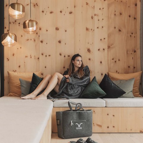 Bilder aus der Sportalm Frau entspannt auf Holzcouch mit Kissen und Wandlampen