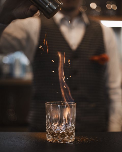 Bilder aus der Sportalm Barkeeper streut Gewürz auf brennenden Drink im Glas