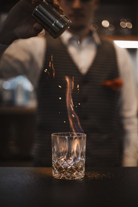 Bilder aus der Sportalm Barkeeper streut Gewürz auf brennenden Drink im Glas