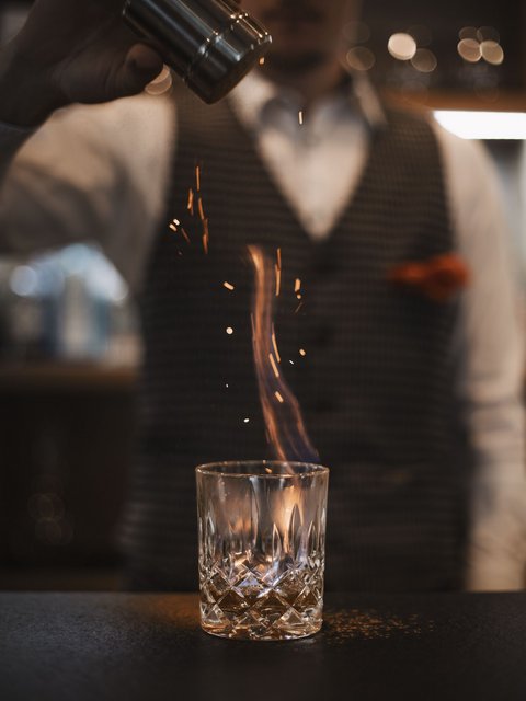 Bilder aus der Sportalm Barkeeper streut Gewürz auf brennenden Drink im Glas