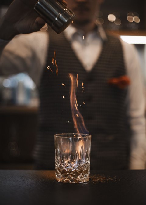 Bilder aus der Sportalm Barkeeper streut Gewürz auf brennenden Drink im Glas