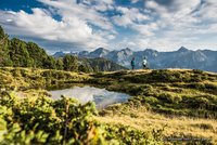 Zwei Wanderer auf einem Bergweg mit See und Alpen im Hintergrund