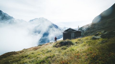 Bilder aus der Sportalm Wanderer auf grasbewachsenem Berg mit Hütte und Nebel in den Alpen