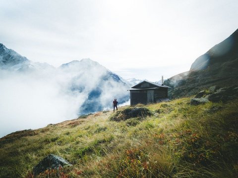 Pictures from Sportalm Hiker on grassy mountain slope with cabin and fog in the Alps