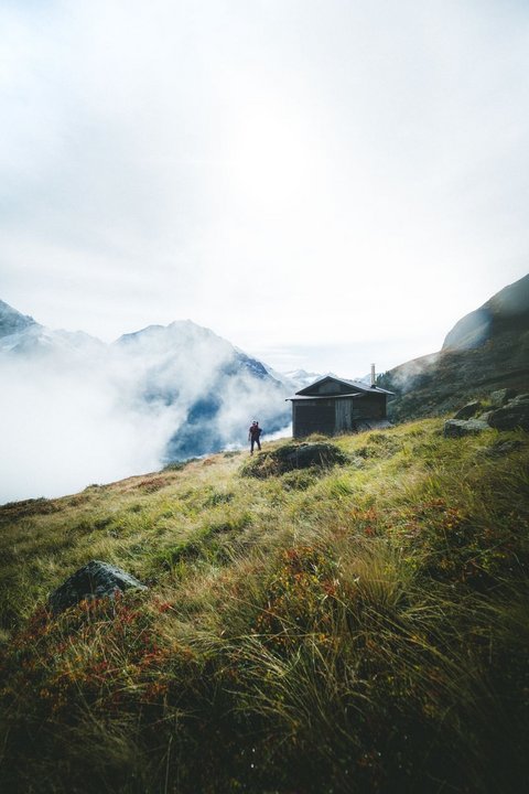 Bilder aus der Sportalm Wanderer auf grasbewachsenem Berg mit Hütte und Nebel in den Alpen