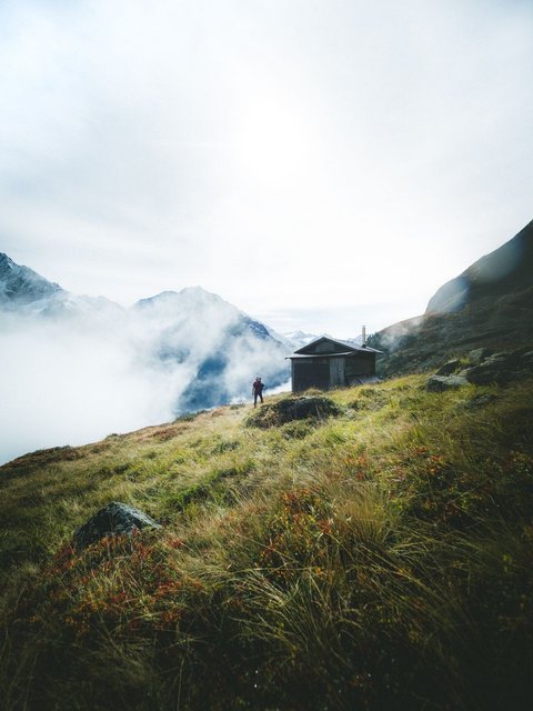 Pictures from Sportalm Hiker on grassy mountain slope with cabin and fog in the Alps