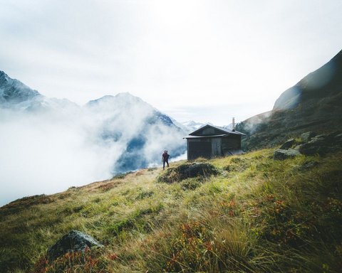 Pictures from Sportalm Hiker on grassy mountain slope with cabin and fog in the Alps