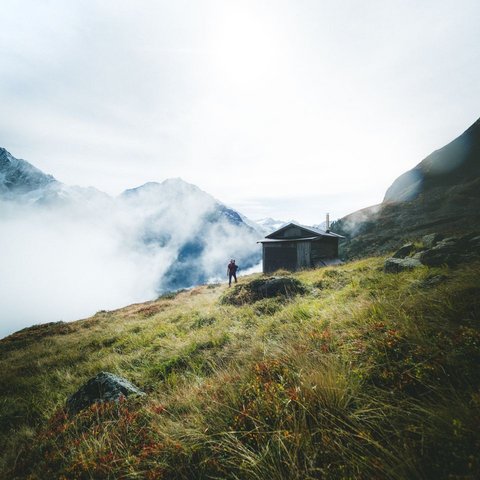 Bilder aus der Sportalm Wanderer auf grasbewachsenem Berg mit Hütte und Nebel in den Alpen