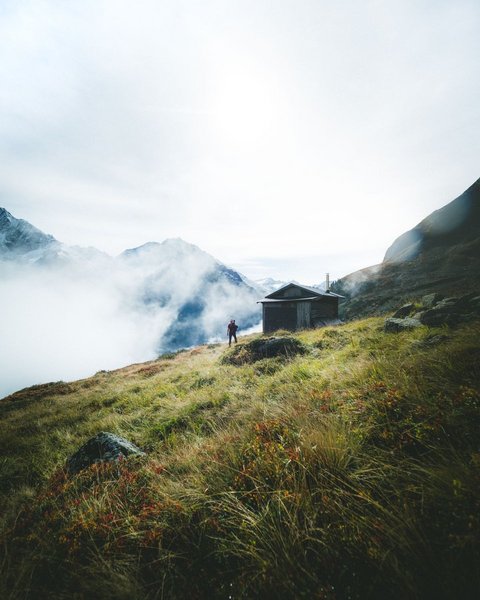 Bilder aus der Sportalm Wanderer auf grasbewachsenem Berg mit Hütte und Nebel in den Alpen