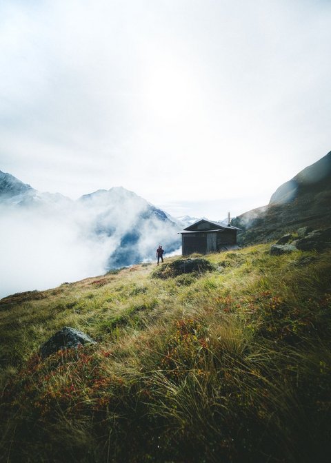 Bilder aus der Sportalm Wanderer auf grasbewachsenem Berg mit Hütte und Nebel in den Alpen