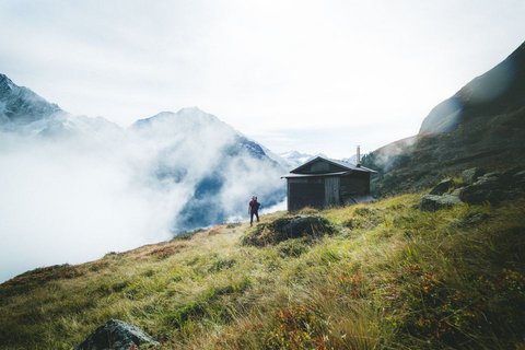 Bilder aus der Sportalm Wanderer auf grasbewachsenem Berg mit Hütte und Nebel in den Alpen