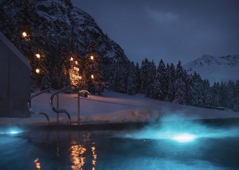 Pictures from Sportalm Lit outdoor pool at night in snowy mountain landscape