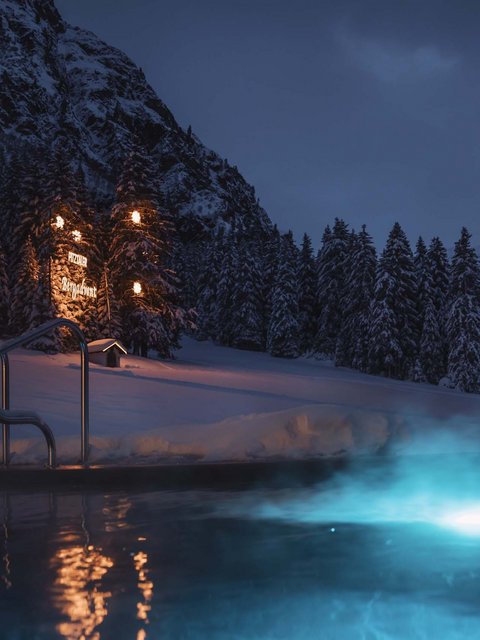 Bilder aus der Sportalm Beleuchteter Außenpool bei Nacht in verschneiter Berglandschaft