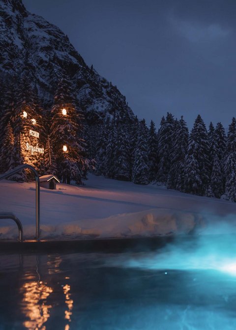 Pictures from Sportalm Lit outdoor pool at night in snowy mountain landscape