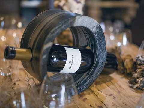 Unser Restaurant im Pitztal Weinflasche in einem steinernen Flaschenhalter auf Holztisch mit Gläsern