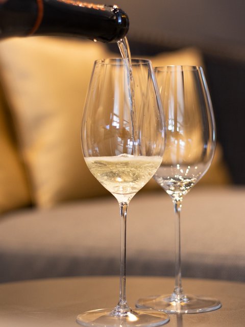 Bilder aus der Sportalm Wein wird in Weinglas eingegossen, Sofa im Hintergrund