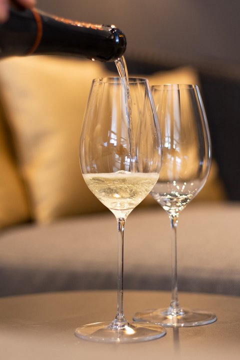 Bilder aus der Sportalm Wein wird in Weinglas eingegossen, Sofa im Hintergrund