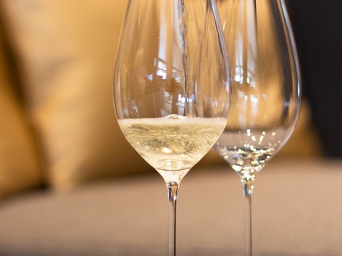 Bilder aus der Sportalm Wein wird in Weinglas eingegossen, Sofa im Hintergrund