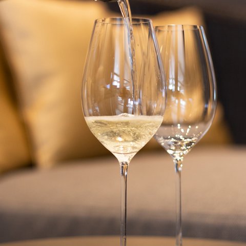 Bilder aus der Sportalm Wein wird in Weinglas eingegossen, Sofa im Hintergrund