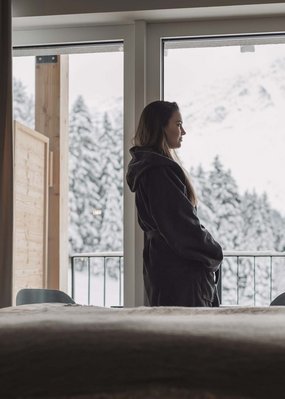 DAS Hotel in St. Leonhard im Pitztal: Alpine Resort Sportalm Frau schaut aus Hotelzimmerfenster auf verschneite Berge und Wald