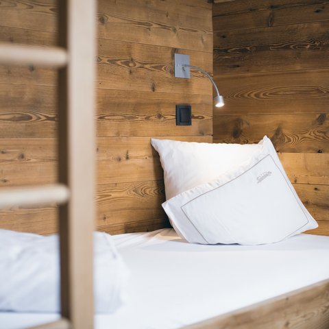 Bilder aus der Sportalm Einzelbett mit weißen Kissen und Holzwand im Hintergrund