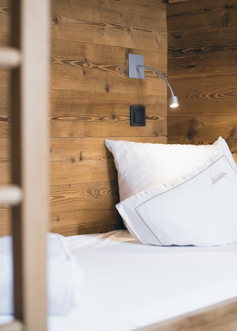 Bilder aus der Sportalm Einzelbett mit weißen Kissen und Holzwand im Hintergrund