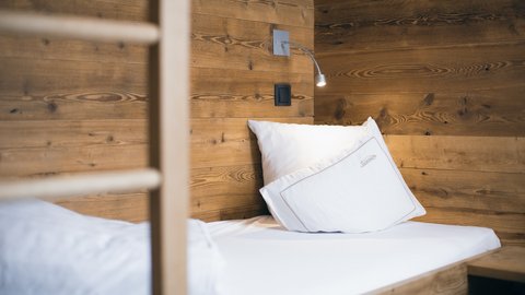 Bilder aus der Sportalm Einzelbett mit weißen Kissen und Holzwand im Hintergrund