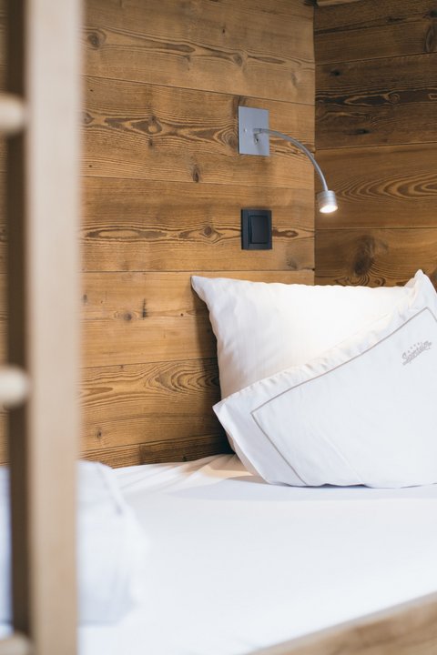 Bilder aus der Sportalm Einzelbett mit weißen Kissen und Holzwand im Hintergrund
